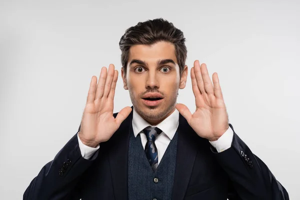 Surprised businessman in suit gesturing while looking at camera isolated on grey — Stock Photo