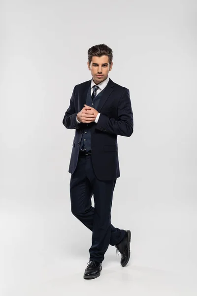 In voller Länge gut aussehender Geschäftsmann im Anzug stehend und in die Kamera blickend auf grau — Stockfoto
