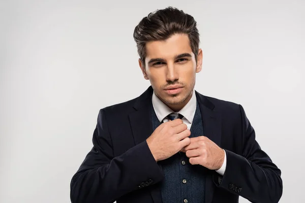Hombre de negocios guapo y joven en traje ajustando corbata aislado en gris - foto de stock