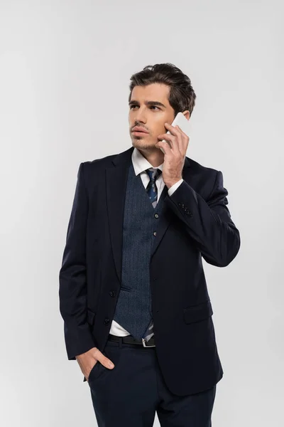 Homme d'affaires confiant en costume debout avec la main dans la poche et parler sur smartphone isolé sur gris — Photo de stock