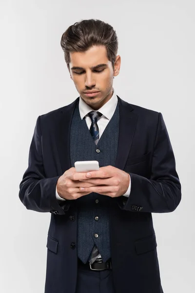 Успешный бизнесмен в костюме обмена сообщениями на смартфоне изолированы на серый — стоковое фото