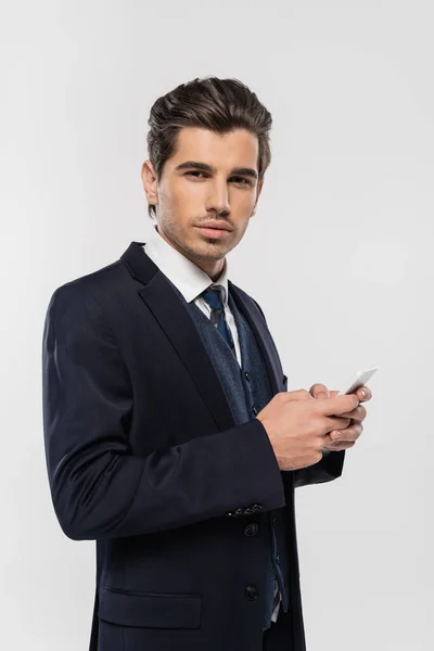 Молодой и успешный бизнесмен в костюмах обмена сообщениями на смартфоне изолирован на серый — стоковое фото