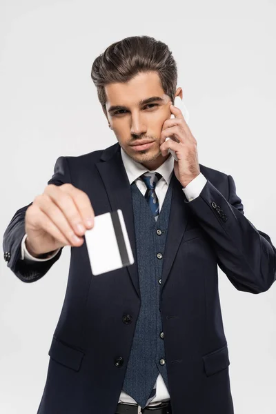 Confident businessman in suit talking on smartphone and holding credit card isolated on grey — Stock Photo
