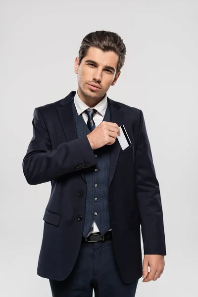 Uomo d'affari di successo in giacca e cravatta mettendo carta di credito in tasca isolato su grigio — Foto stock
