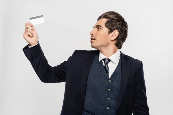 Молодой бизнесмен в костюме глядя на кредитную карту изолированы на серый — стоковое фото