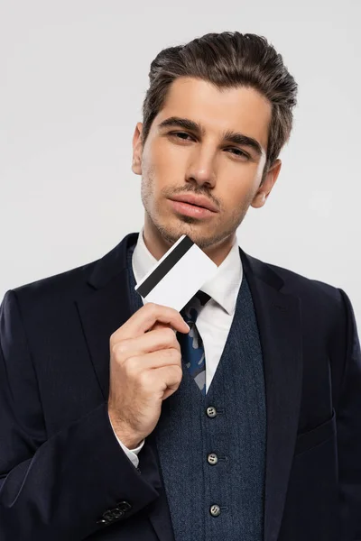 Exitoso hombre de negocios en traje con tarjeta de crédito y mirando a la cámara aislada en gris - foto de stock