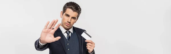 Erfolgreicher Geschäftsmann im Anzug hält Kreditkarte in der Hand und zeigt Stopp-Geste isoliert auf grauem Banner — Stockfoto