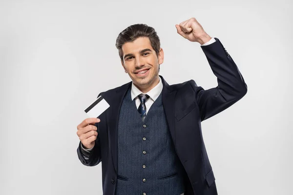 Щасливий бізнесмен з брекетами тримає кредитну картку і дивиться на камеру ізольовано на сірому — стокове фото
