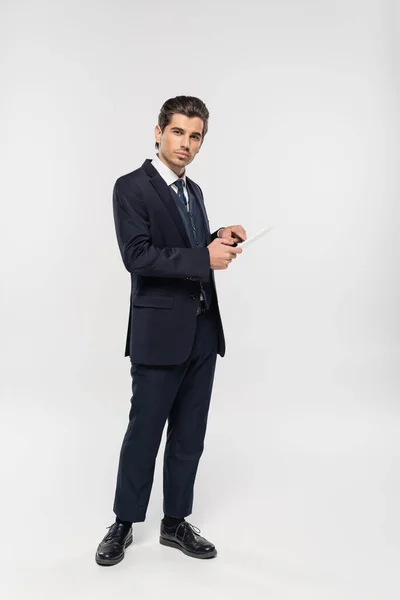 Повна довжина молодого бізнесмена в костюмі тримає цифровий планшет на сірому — стокове фото