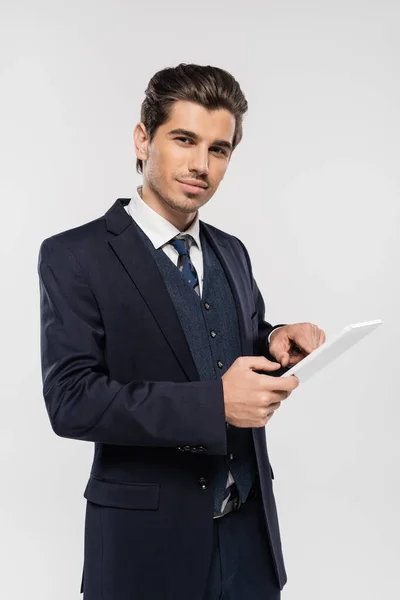 Cheerful young businessman in suit holding digital tablet isolated on grey — Stock Photo