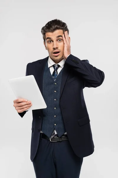 Stressed young businessman in suit holding digital tablet isolated on grey — Stock Photo