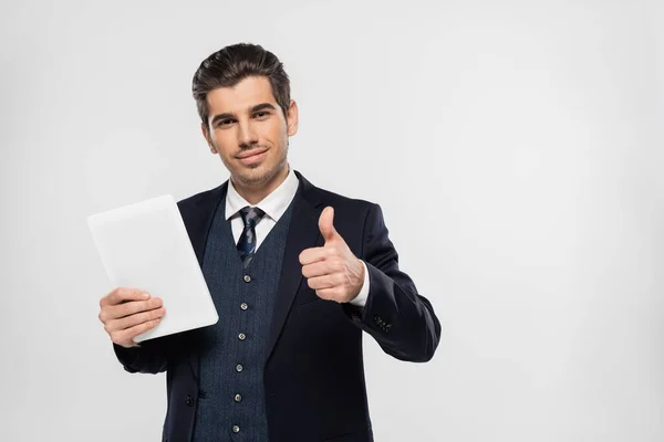 Fröhlicher junger Geschäftsmann im Anzug hält ein digitales Tablet in der Hand und zeigt den Daumen vereinzelt auf grau — Stockfoto