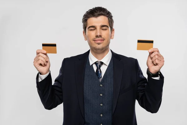 Молодий бізнесмен із закритими очима тримає кредитні картки ізольовані на сірому — стокове фото
