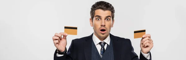 Sorprendido hombre de negocios en traje con tarjetas de crédito aisladas en gris, bandera - foto de stock
