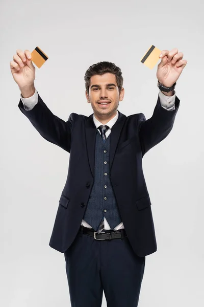 Allegro uomo d'affari in giacca e cravatta con carte di credito isolate su grigio — Foto stock