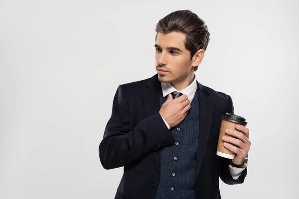 Молодой бизнесмен держит бумажную чашку, регулируя галстук изолирован на серый — стоковое фото