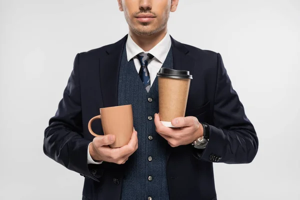 Cropped view of businessman holding paper cup and mug isolated on grey — Stock Photo