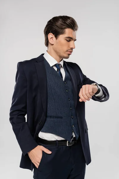 Giovane uomo d'affari in abbigliamento formale guardando orologio da polso isolato su grigio — Foto stock