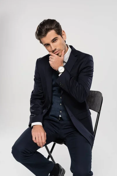 Молодий бізнесмен у формальному одязі, сидячи на стільці, позує ізольовано на сірому — стокове фото