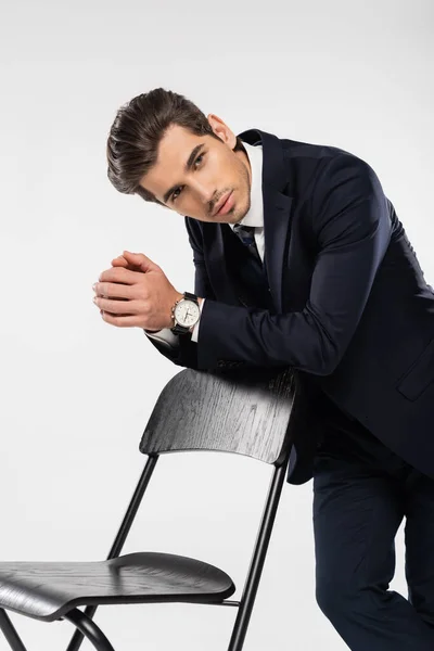 Uomo d'affari di successo in abbigliamento formale in piedi vicino sedia isolata su grigio — Foto stock