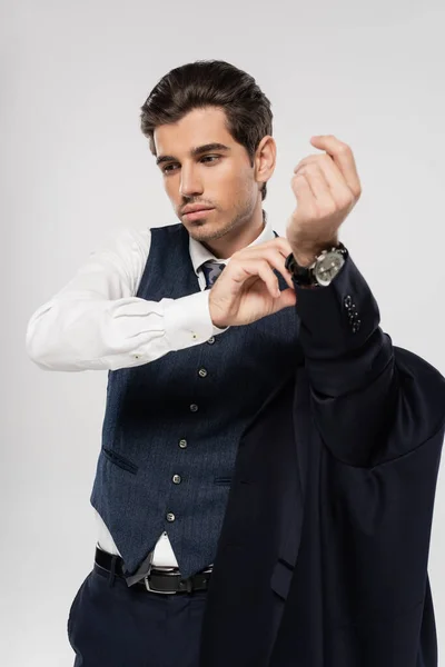Hombre de negocios en traje quitándose la chaqueta y ajustando el reloj de pulsera aislado en gris - foto de stock