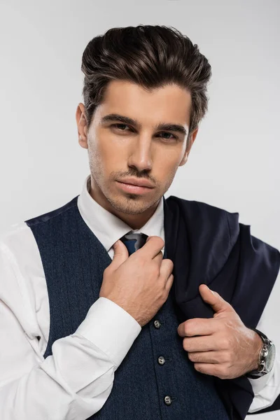 Homme d'affaires en tenue formelle tenant blazer et ajustant cravate isolé sur gris — Photo de stock