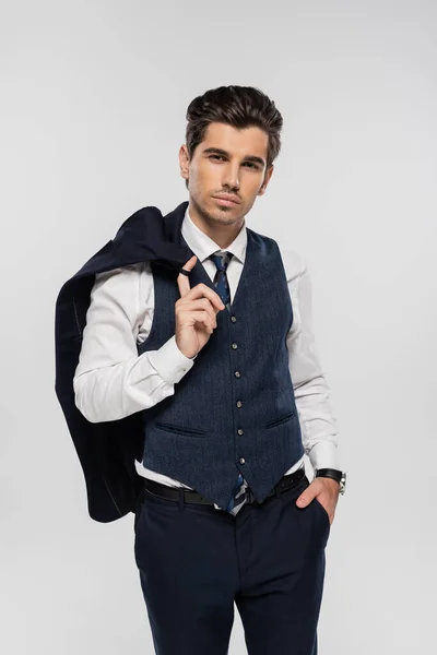 Бізнесмен в офіційному одязі тримає блейзер і стоїть з рукою в кишені ізольовано на сірому — стокове фото