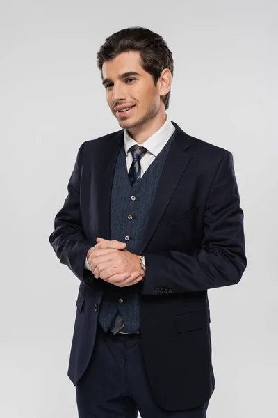 Cheerful businessman in formal wear smiling and standing with clenched hands isolated on grey — Stock Photo