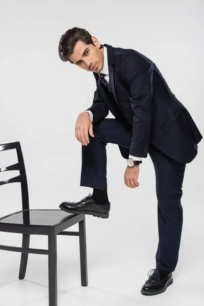 Geschäftsmann in voller Länge in formeller Kleidung tritt auf Stuhl auf grau — Stockfoto