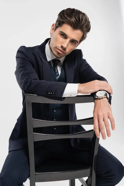 Hombre de negocios en ropa formal sentado mientras se apoya en la silla aislado en gris - foto de stock