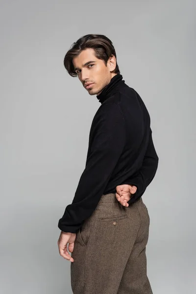 Good looking man in black turtleneck and pants looking at camera isolated on grey — Stock Photo