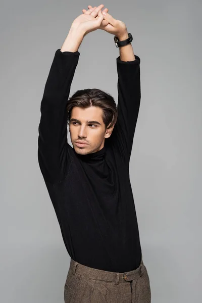 Young good looking man in black turtleneck posing with raised hands isolated on grey — Stock Photo