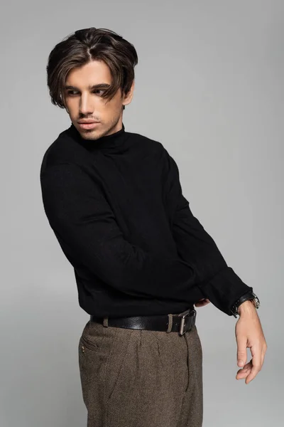 Brunette young man in black turtleneck posing and looking away isolated on grey — Stock Photo