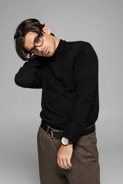 Brunette model in black turtleneck and pants posing in eyeglasses isolated on grey — Stock Photo