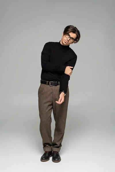 Brune pleine longueur homme en col roulé noir et pantalon posant en lunettes sur gris — Photo de stock