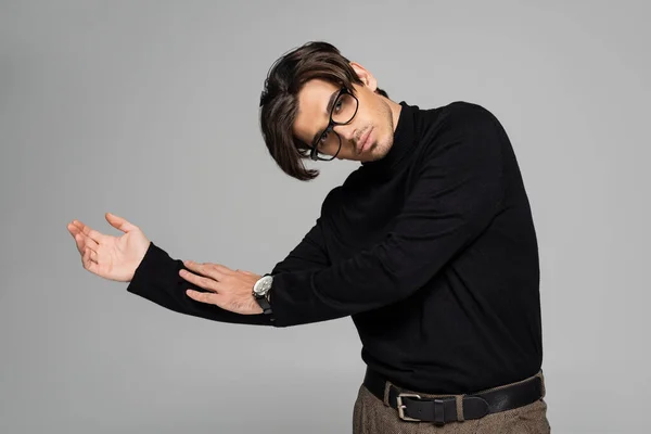 Junger Mann mit schwarzem Rollkragen und Brille blickt in die Kamera, während er isoliert auf grau posiert — Stockfoto