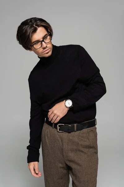 Brunetta uomo in dolcevita nero e pantaloni in posa in occhiali isolati su grigio — Foto stock