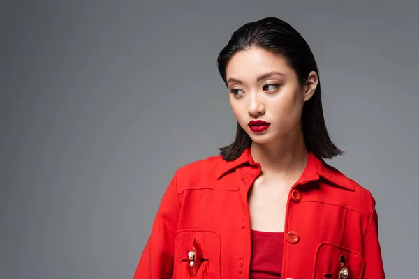 Portrait of brunette asian woman in red fashionable jacket isolated on grey — Stock Photo
