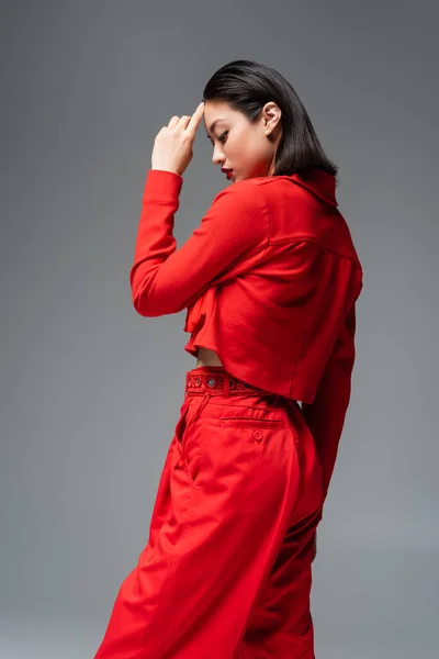 Seitenansicht einer asiatischen Frau in roter stylischer Kleidung, die Stirn in grau isoliert berührt — Stockfoto