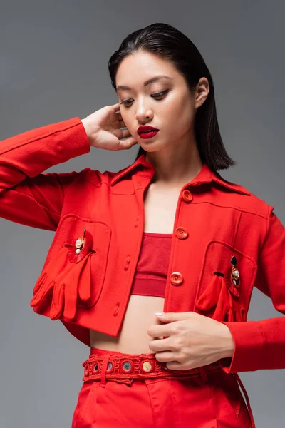 Young asian model in red blazer decorated with brooches and gloves isolated on grey — Stock Photo