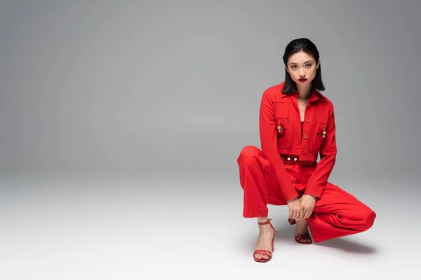 Молодая азиатская модель в красном элегантном костюме и сандалиях, позирующая на сером фоне — стоковое фото
