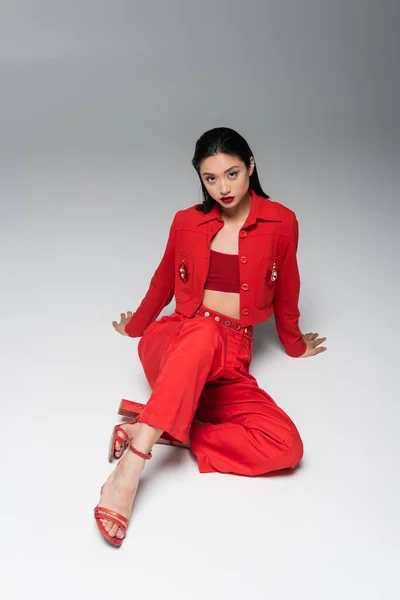 Sinnliche asiatische Frau in rotem Anzug und hochhackigen Sandalen auf grauem Hintergrund — Stockfoto