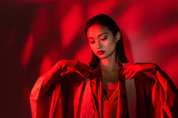 Элегантная азиатка в перчатках и кимоно на красном фоне с тенью — стоковое фото
