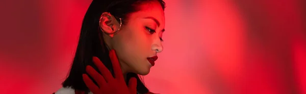 Портрет азиатки в перчатке и ушной манжете на абстрактном фоне с красным светом, баннер — стоковое фото