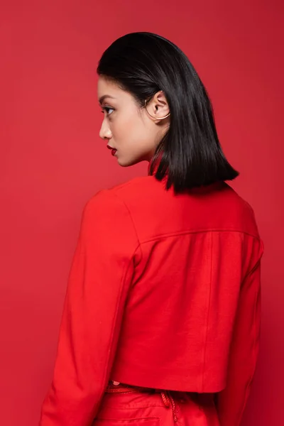 Young asian woman in trendy blazer and ear cuff looking away isolated on red — Stock Photo