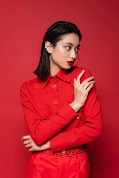 Молода азіатка з макіяжем позує в модній куртці і дивиться ізольовано на червоний — стокове фото