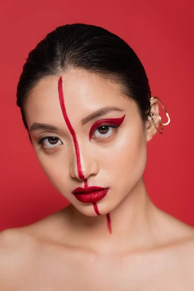 Retrato de mujer asiática con puño de oído elegante y rostro artístico mirando a la cámara aislada en rojo - foto de stock