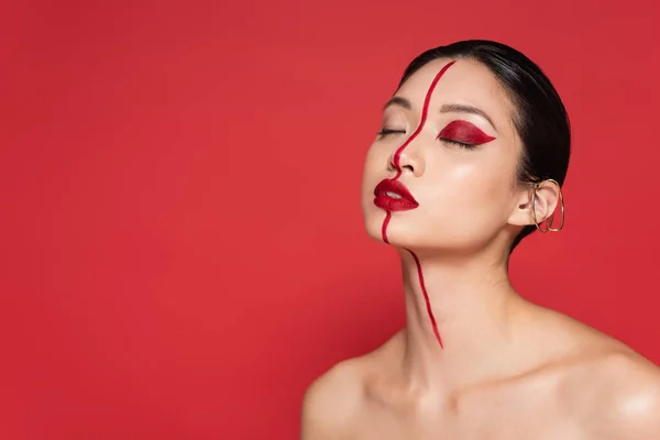 Retrato de mujer asiática con los ojos cerrados y maquillaje artístico aislado en rojo - foto de stock