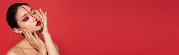 Sensual asiático mulher com nua ombros e artístico visage tocando perfeito rosto com fechado olhos isolado no vermelho, banner — Fotografia de Stock