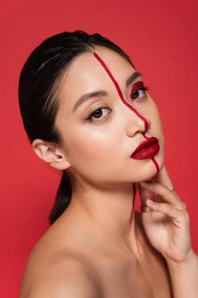 Porträt eines asiatischen Models mit kreativem Aussehen und perfekter Haut, die die Hand nahe am Gesicht hält und isoliert auf Rot in die Kamera blickt — Stock Photo